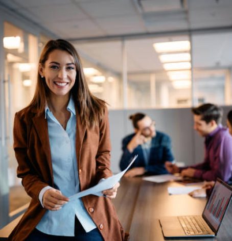 Young happy executive manager holding business meeting with her coworkers in the office and looking at camera.